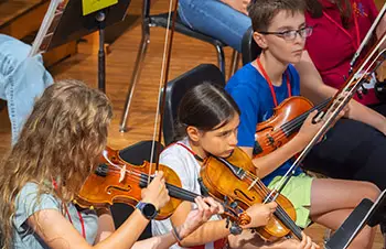 three students playing violins